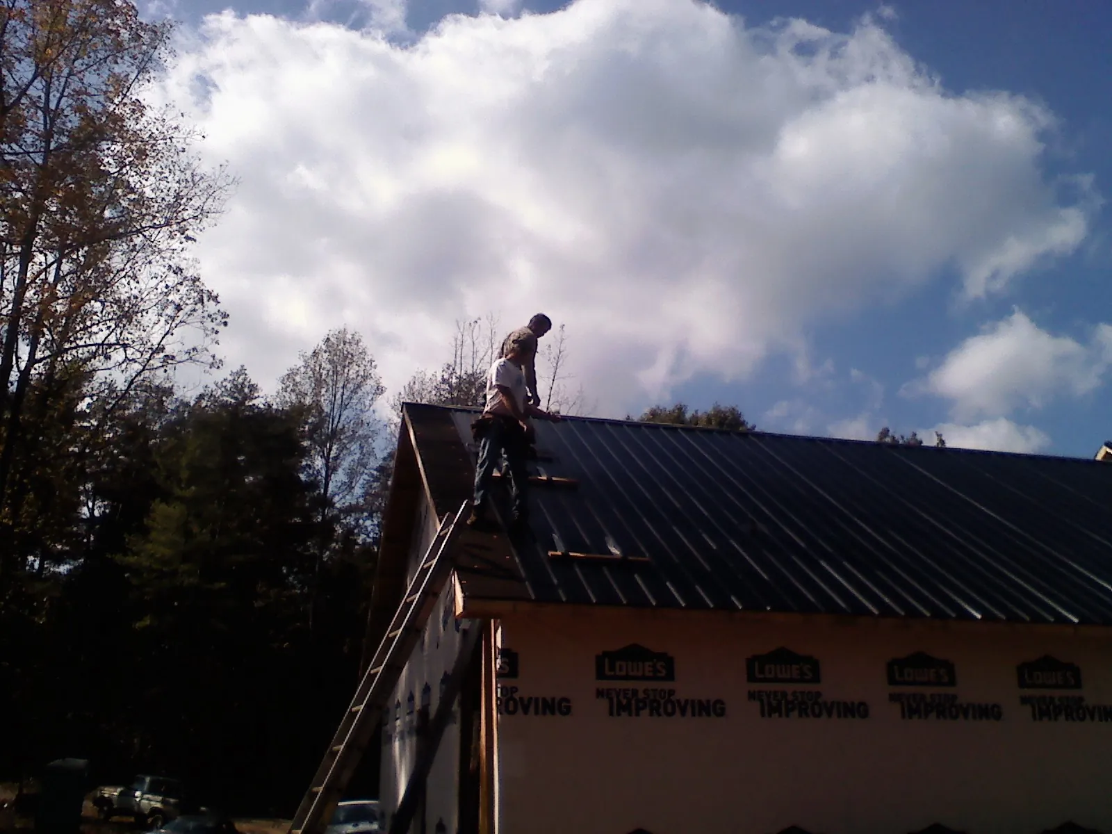 Roofer fastening dark metal panels high against a cloudy sky, from a Roof Inspection job in Brinnon