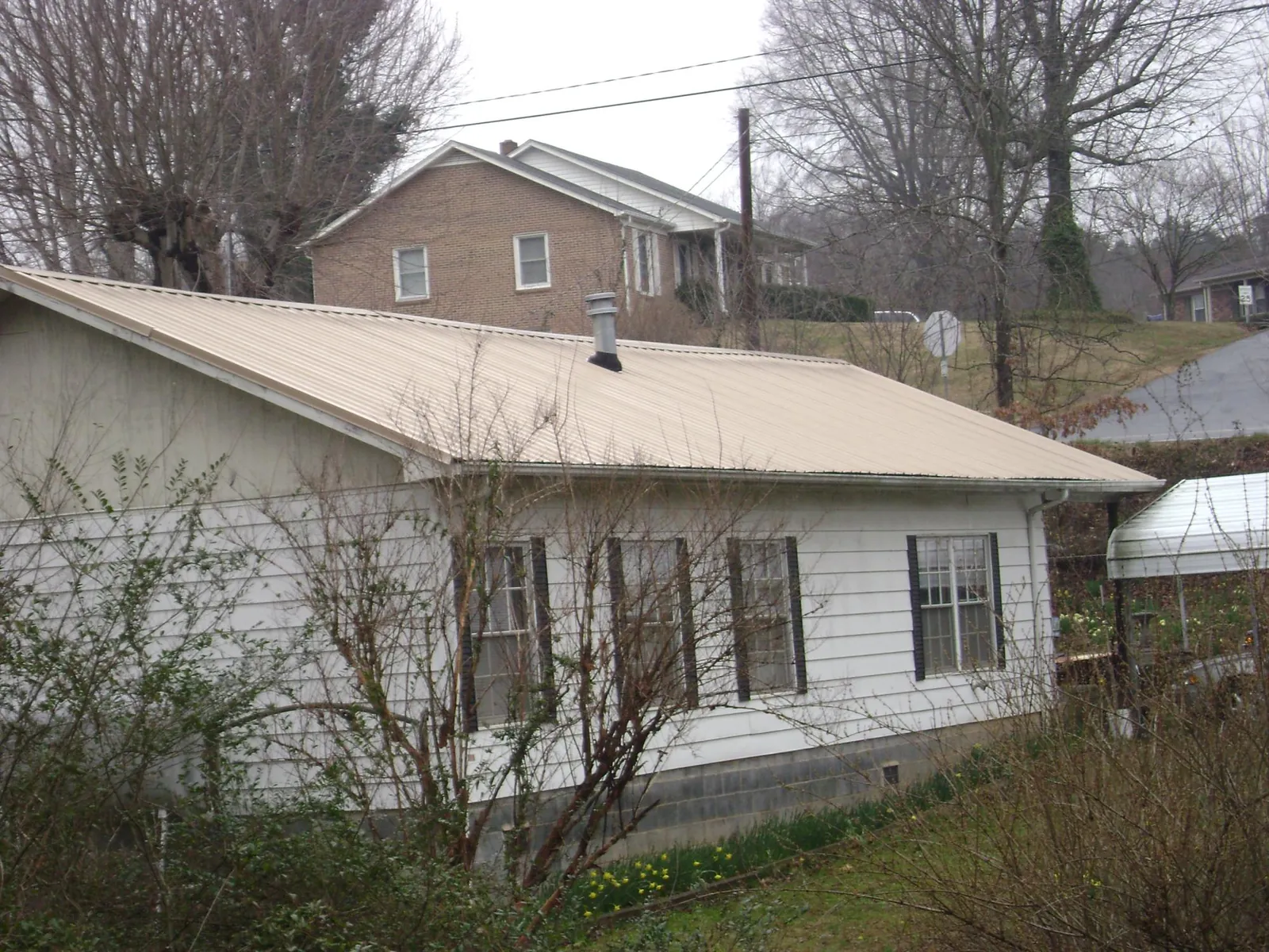 Tan metal roof on a white sided house set into a hillside — Commercial Roofing by Roofing Brothers in Brinnon